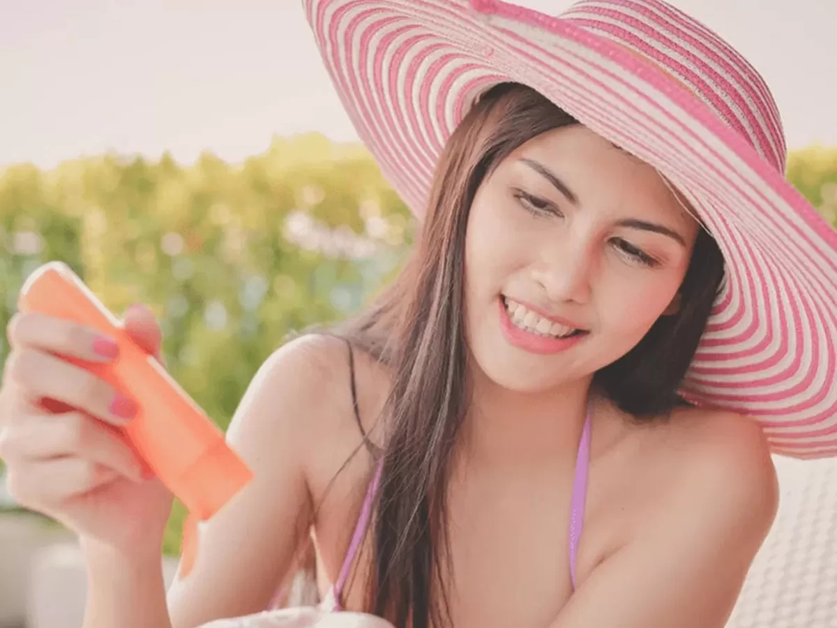 female applying mineral sunscreen and wearing sun hat