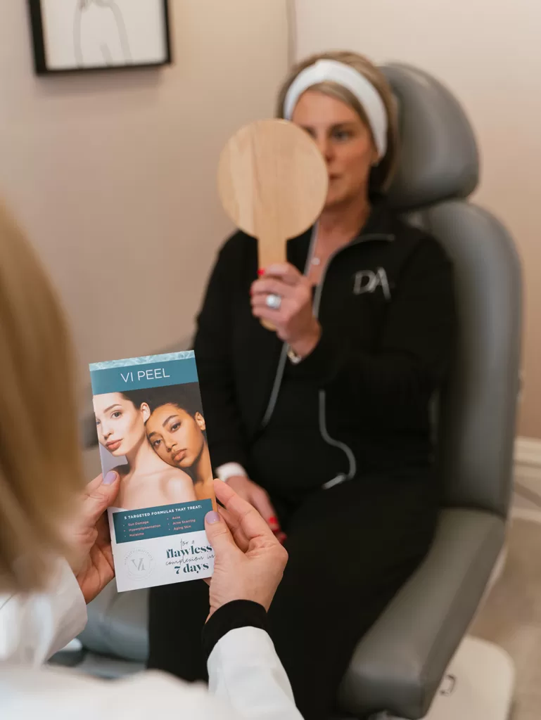 Female holding a mirror looking at her face after a chemical peel