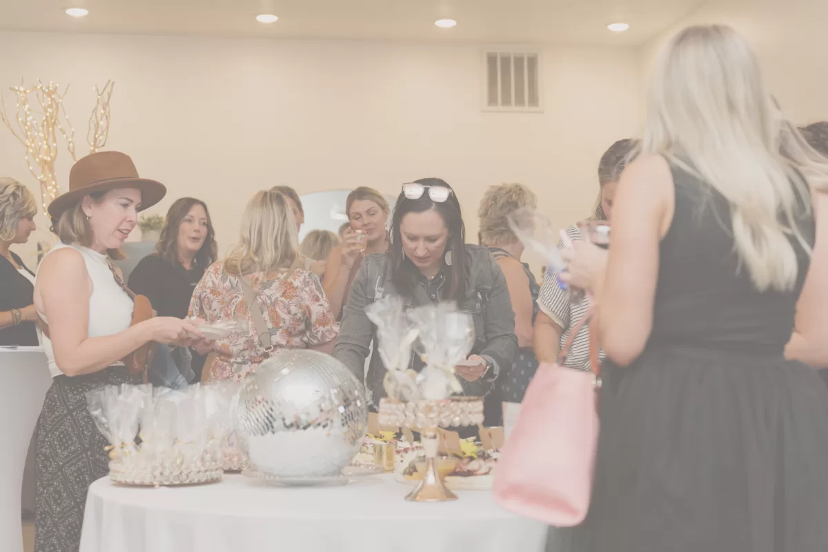 group of people standing around the giveaway table at an event
